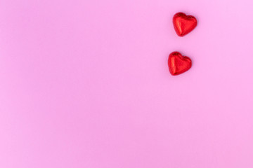 Heart-shaped chocolates are on the pink background. Flat lay. Copy space.