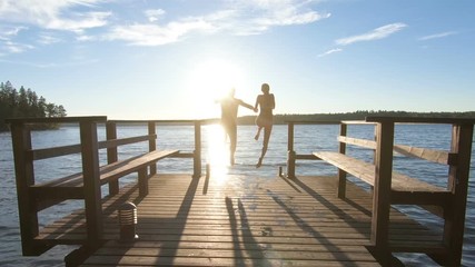 couple running on a wooden pier and jumping into the lake after the sauna in summer white night in Finland.
