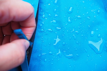 Selective focus of water drops on bright blue fabric and black zipper with waterproof design to...
