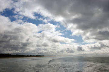 Panoramic view of heavy storm clouds with some blue sky patches over a wide beach and ocean waters on a California winter day