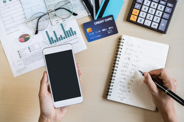 Young woman using smart phone and checking bills, taxes, bank account balance and calculating expenses in the living room at home