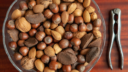Assortment of whole nuts, walnuts, almonds, hazelnuts and Brazil nuts in a bowl with a nut cracker on a side, nutritious snack cracked and eaten in autumn or winter months as a special holidays treat.