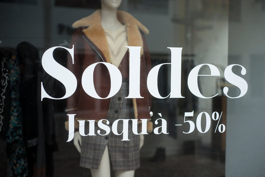 closeup of discount sign "SOLDES jusqu'a 50%" in french,  the traduction of  (sales until 50%) on window in french fashion store showroom on winter clothes background