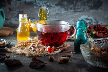 Red Hot Hibiscus tea in a glass mug on a wooden table among rose petals and dry tea custard with metallic heart