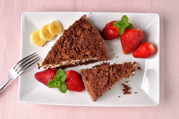 Mole hole cake - homemade cake with whipped cream, banana, strawberries and fresh mint leaves on white decorative shaped plate. Pink place setting. Top view.