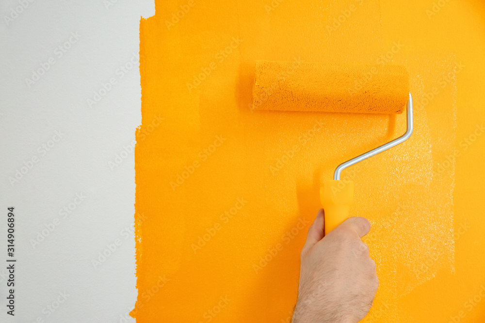 Poster Man painting white wall with yellow dye, closeup. Interior renovation