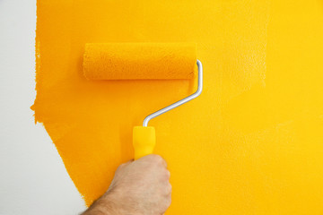 Obraz premium Man painting white wall with yellow dye, closeup. Interior renovation