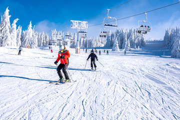 People enjoying skiing and snowboarding in mountain ski resort with beautiful winter landscape in the background - obrazy, fototapety, plakaty