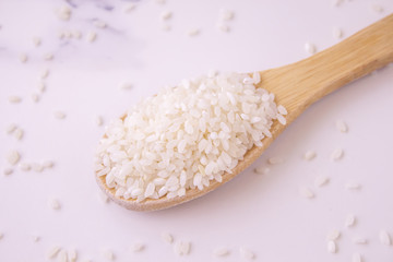  rice wooden spoon on white marble background. close-up, sprinkled rice