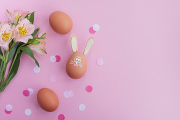 Easter eggs with bunny ears and flowers on light pink background. Minimal composition. Top view, flat lay, copy space