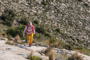 Woman hikes along ridgecrest walks up hill, El Divino mountain, Alicante province, Costa Blanca, Spain