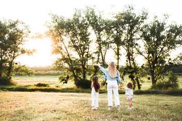 Naklejka na ściany i meble Blonde mother with two cute daughters are walking and having fun outdoors. Stylish, casual clothes.