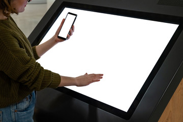 Woman with phone uses self-service kiosk in the shopping mall