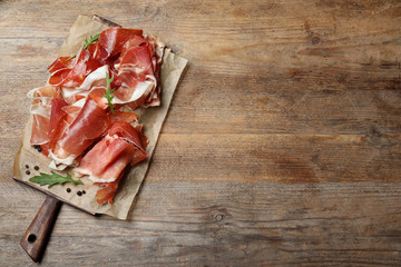 Pile of tasty prosciutto on wooden table, top view. Space for text