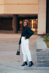 Beautiful young black african muslim girl wearing a bandana on the street of modern city. She is standing with a happy smile on her face. Human emotions, facial expression concept. Fashion colors