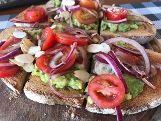 oasted bread with avocado guacamole with tomato and finely chopped red onion, vegan lunch in restaurant vegetarian dish