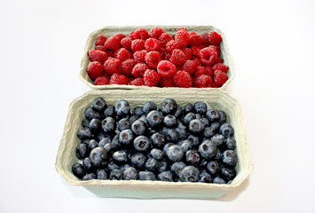 Background of sweet raspberry and blueberry in packing containers, cardboard boxes with berries. Red and blue fruit in package, closeup. Healthy, delicious dessert in packaging.