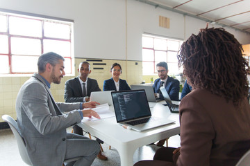 Confident boss talking to subordinates. Smiling relaxed workers sitting at table and listening to boss. Business meeting concept