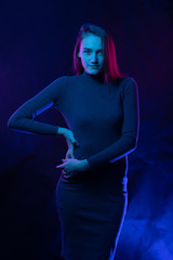 Young beautiful model in sweater in colored light, colored neon lamps blue and purple.