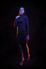 High Fashion model woman in colorful bright lights posing full length, standing on his feet in studio. young woman in multicolor lights. on a black background.