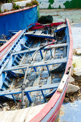 Fototapeta na wymiar Old and broken little small fishing boat. Rotting wood but still preserved color lines. White blue and red. The boat is parked in an empty pool. served as a decoration in front of the restaurant.