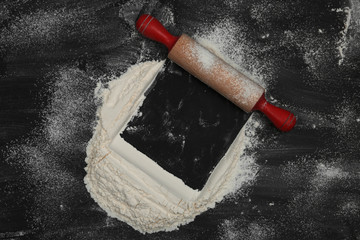 Flour and rolling pin on black table, top view. Space for text