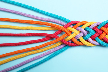 Braided colorful ropes on light blue background, top view. Unity concept