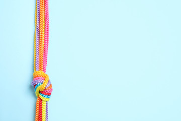 Top view of colorful ropes tied together on light blue background, space for text. Unity concept