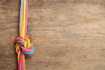 Top view of colorful ropes tied together on wooden background, space for text. Unity concept
