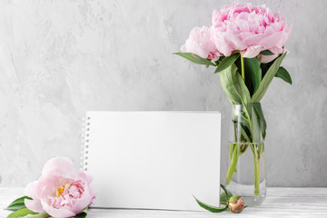 Obraz na płótnie Canvas pink peony flowers bouquet with blank greeting card or wedding invitation on white table with copy space. mock up