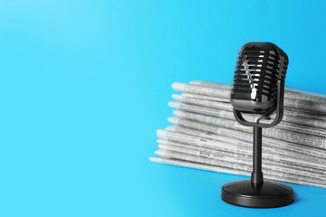 Newspapers and vintage microphone on light blue background, space for text. Journalist's work