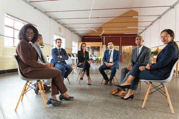 Business people sitting in chairs in circle. Confident employees looking at camera. Teambuilding concept