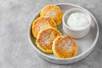 Cottage cheese pancakes or syrniki with sour cream on hand-made ceramic plate