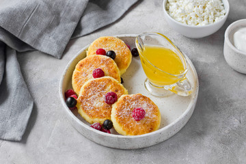 Cottage cheese pancakes or syrniki with honey, raspberry, blackcurrant and sour cream on hand-made ceramic plate