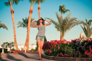 happy woman in shorts jeans and hat walking at the hotel near palm trees background. Concept time...