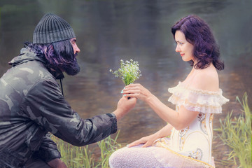 a man with a beard and a hat gives flowers to a girl in a dress and corset