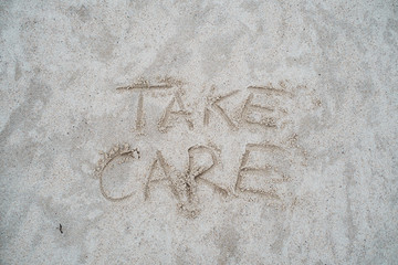 Take care sign drawn on beach sand.