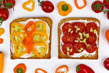 Top view on slices of healthy whole grain toast topped with vegetables like yellow and orange bell pepper and cherry tomatos