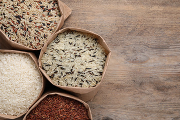 Different types of brown and polished rice in paper bags on wooden table, flat lay. Space for text