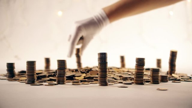 The concept of money. Columns of gold coins in the form of skyscrapers or Stonehenge. Close-up hands make up stacks of coins. Smoke. Garland.