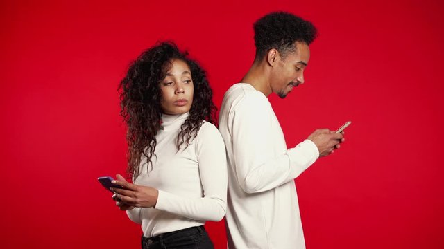 Couple stand with their backs to each other, printing messages or surf Internet. Woman is peeking over her boyfriends shoulder, while he is communicating via mobile telephone. Trick concept.