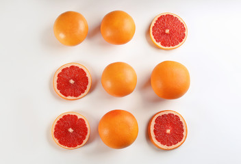 Fototapeta na wymiar Cut and whole ripe grapefruits on white background, flat lay