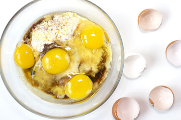 Corn and rice flour, coconut sugar, four eggs in the transparent plate. Making a cake. Mixing the dough. White background. Copy space. Place for text and design. Top view. Flat lay. Gluten-free recipe