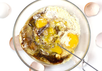 Corn and rice flour, coconut sugar, four eggs in the transparent plate. Making a cake. Mixing the dough. White background. Copy space. Place for text and design. Top view. Flat lay. Gluten-free recipe