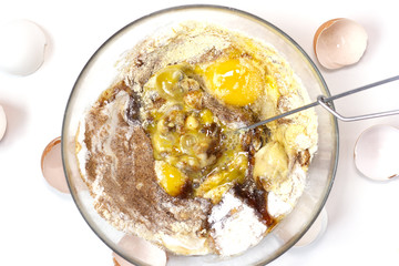 Corn and rice flour, coconut sugar, four eggs in the transparent plate. Making a cake. Mixing the dough. White background. Copy space. Place for text and design. Top view. Flat lay. Gluten-free recipe