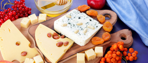 Cheese platter: variety of cheeses on wooden plate with fruits and nuts. Different types of cheese and honey. Hard cheese and berries on a classic blue background. Top view