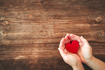 top view of woman hands holding red heart on wooden table.
