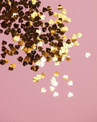 Lots of sequins in the shape of Golden hearts on a pink background. Card with plenty of space for text input, the theme of love. Vertical photo.