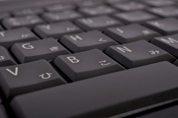 Japanese computer or laptop keyboard. Symbols on the buttons of hiragana. Teaching Japanese language and writing. Dark background or wallpaper. Low contrast