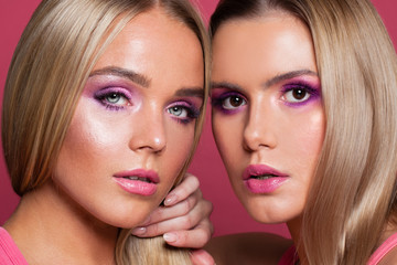 Glamorous women models with fashion makeup on pink background close up portrait
